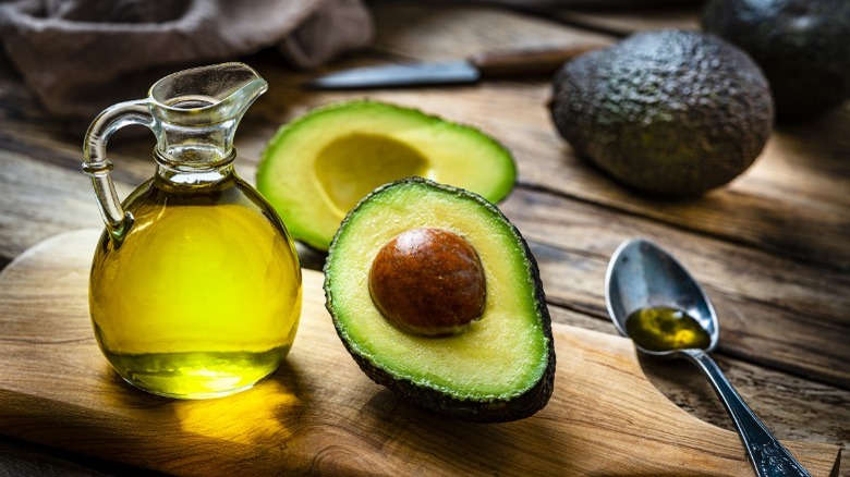 Avocado oil in a vessel with a halved avocado next to it