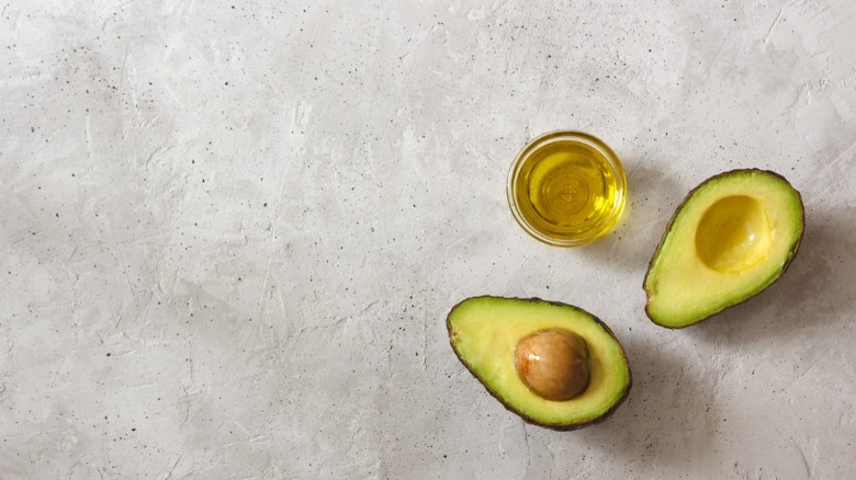 Cut avocado next to avocado oil in a small glass bowl
