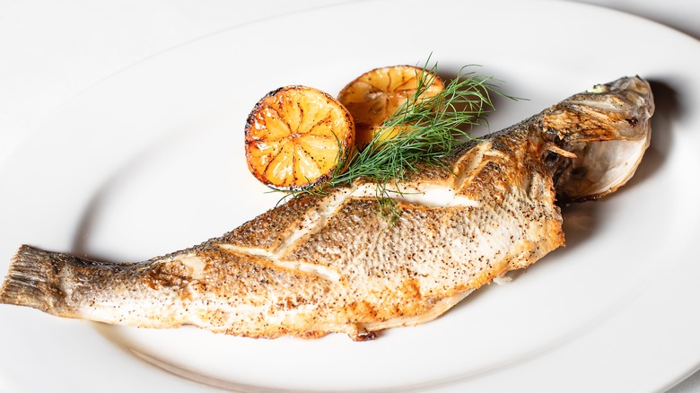 Whole roast branzino on plate with citrus wedges