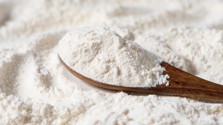 A wooden spoon of flour resting on a bed of flour