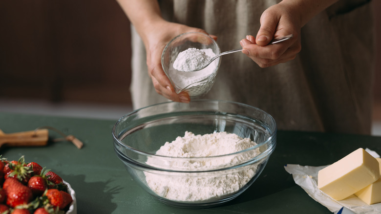 A baker measuring flour into a glass bowl