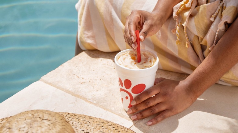 Someone sits poolside, stirring a milkshake.