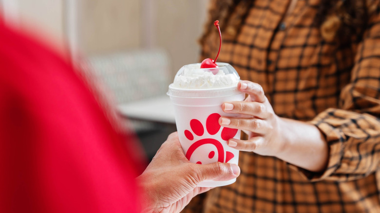 A Chick-fil-A employee hands a customer a milkshake.