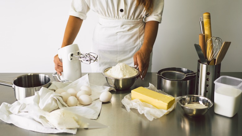 A baker with ingredients like flour, butter, and eggs on a stainless steel counter