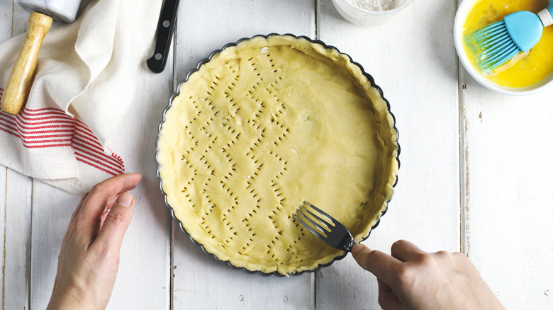A person scores a pie crust in a zig-zag pattern using a fork