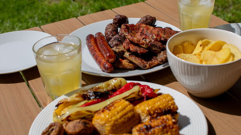 A backyard cookout spread with grilled hot dogs, meat, corn and potato chips