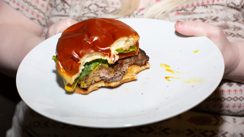 A woman holds a plate containing a half-eaten well-done burger