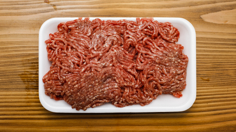 Ground beef sits in a white styrofoam tray on a wooden surface