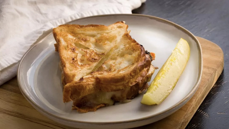 Croissant bread grilled cheese with pickle on plate.