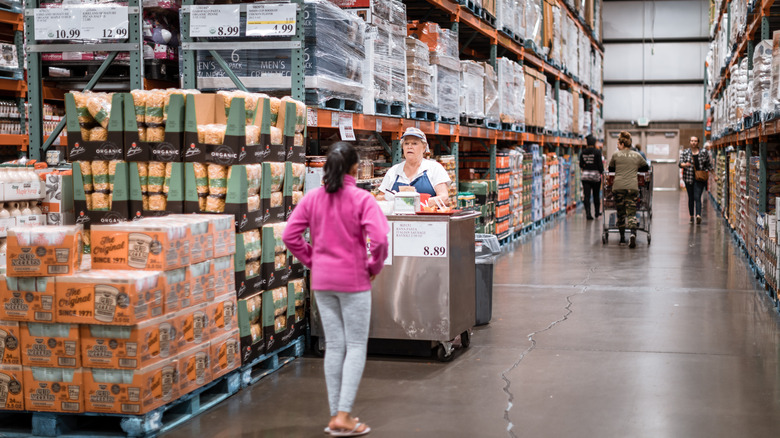 Costco shopper approaching sample cart in aisle.