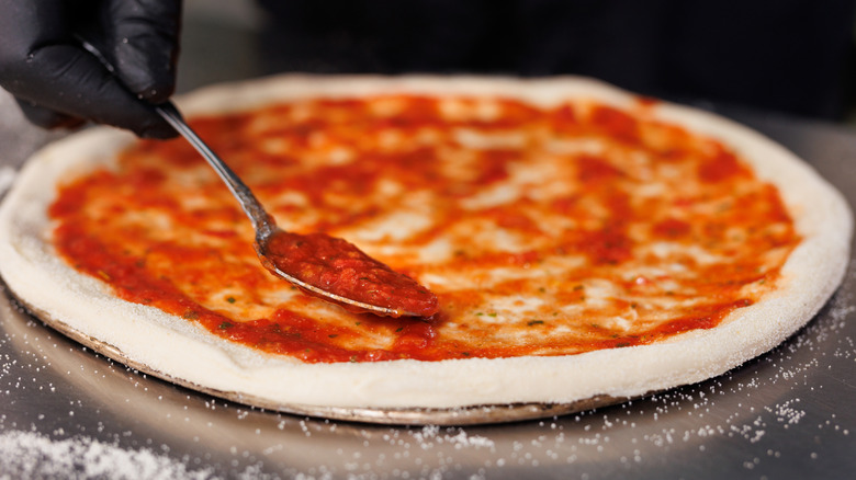 Chef spreading sauce on pizza dough