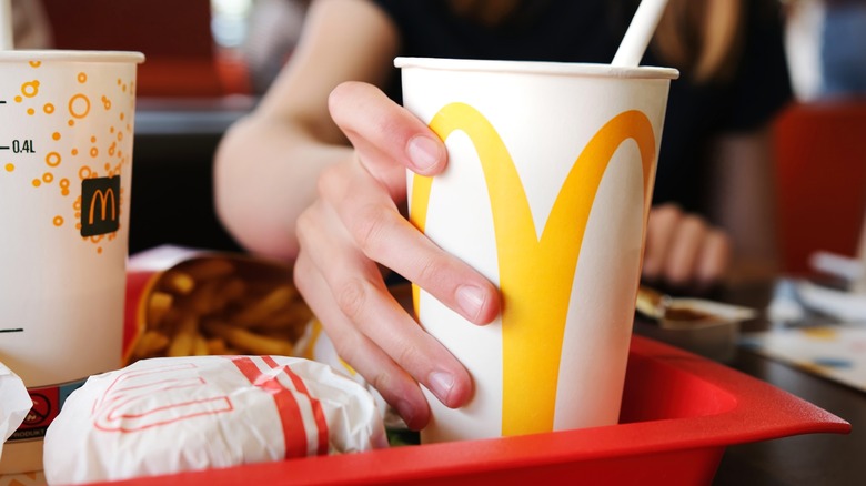 A female hand grasps a McDonald's soda cup on a plastic restaurant tray containing other food and drink items