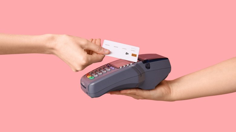 A hand holds a credit card over a payment device that is held out by another hand