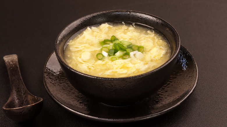 egg drop soup in a black bowl on black background