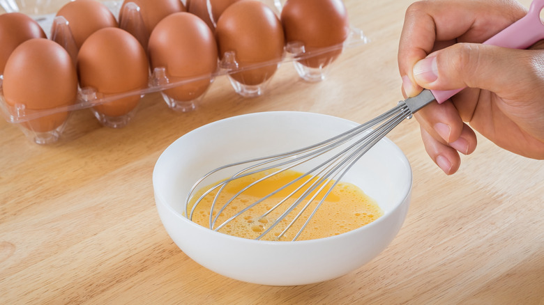 male hand whisking eggs in white bowl