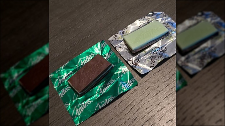A regular Andes Mint and a specialty Olive Garden Andes Mint sit side by side, unwrapped and sitting on their wrappers.