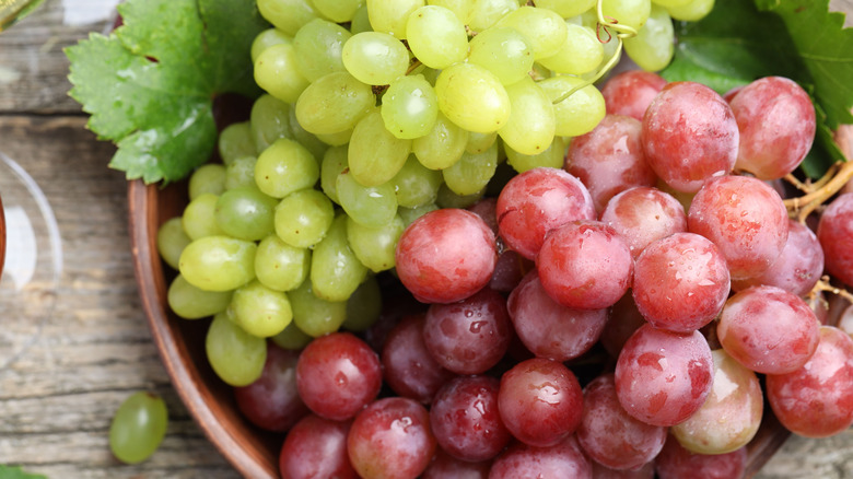 Ripe green and red grapes in a wooden bowl.