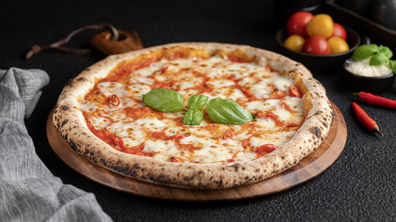 A homemade cheese pizza topped with basil on a pizza stone