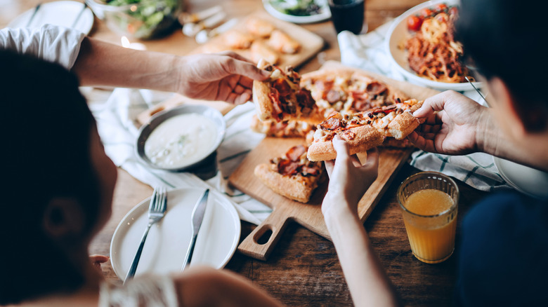 Friends pulling slices of homemade pizza from a charcuterie board