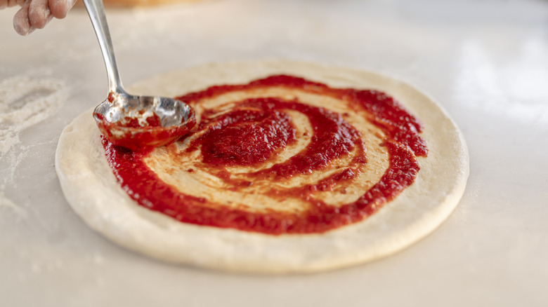 Chef spreading marinara over pizza dough