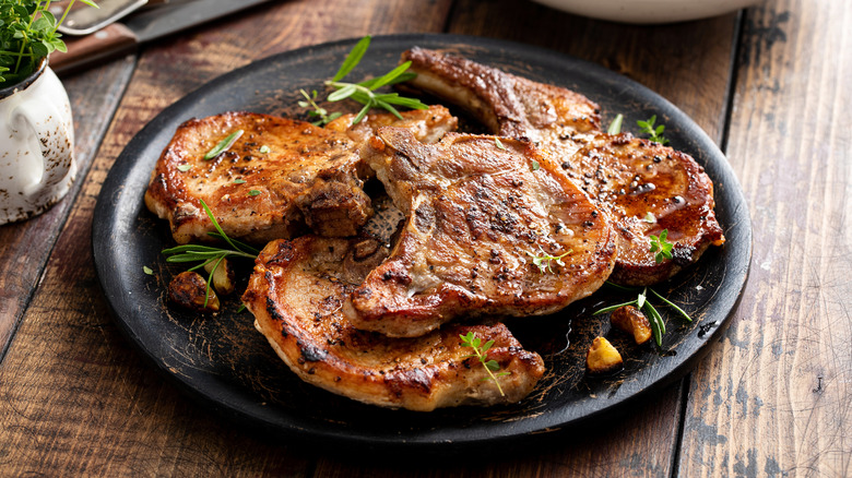 A pile of cooked bone-in pork chops on a black stone plate