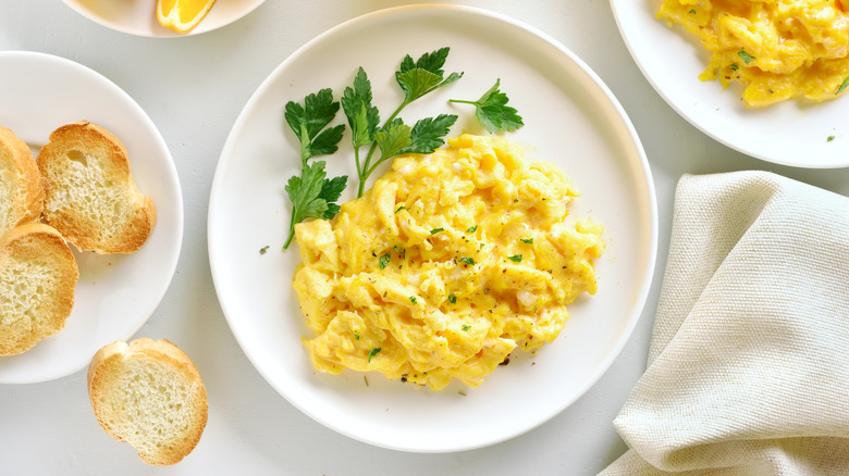 fluffy scrambled eggs on white plate with herbs
