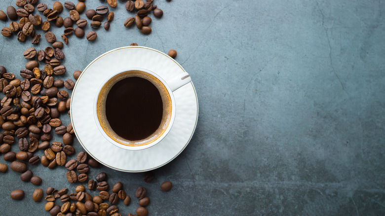 cup of coffee on dark surface with whole coffee beans