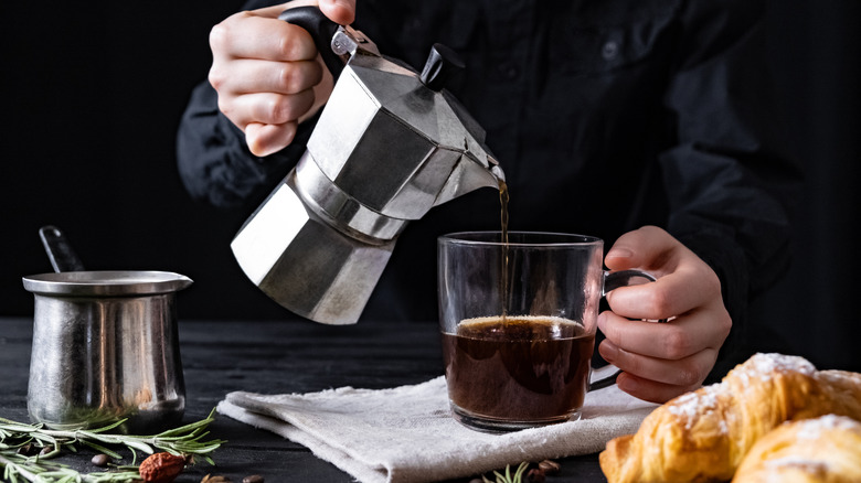 Person pouring coffee from a moka pot percolator into a cup
