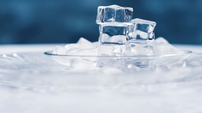 Clear ice cubes stacked in a bowl of ice with a dark blue background