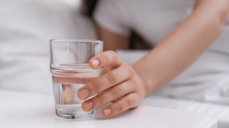 person reaching for glass of water on nightstand