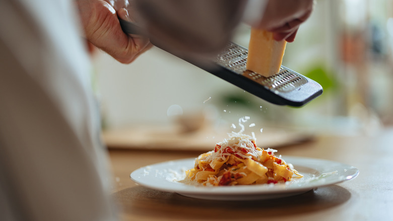 Hands grating parmesan cheese over dish of pasta