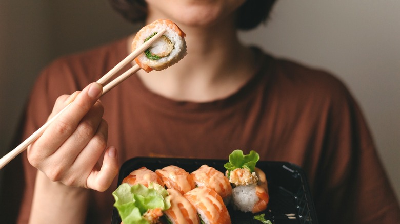 Woman holding chopsticks and a tray of sushi