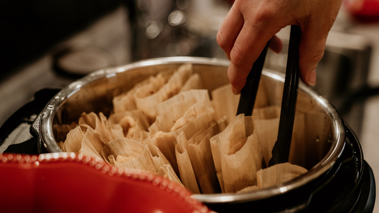 tongs being used to pull tamales from pot