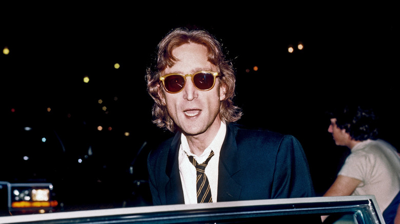 John Lennon wearing sunglasses as he emerges from a car at a recording studio.