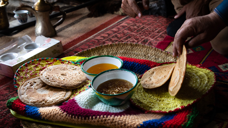 hand grabbing flatbread with bowls of ghee and honey