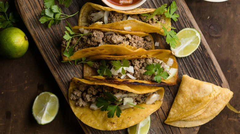 Four tacos next to limes on a wooden board