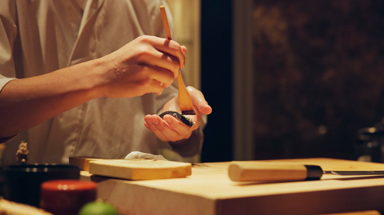 Japanese sushi chef painting sauce on to a piece of fish