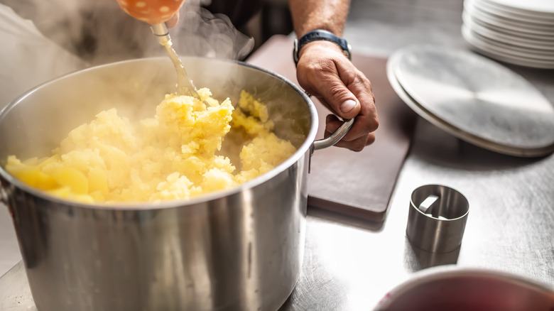 A man mashes potatoes in a big stock potA