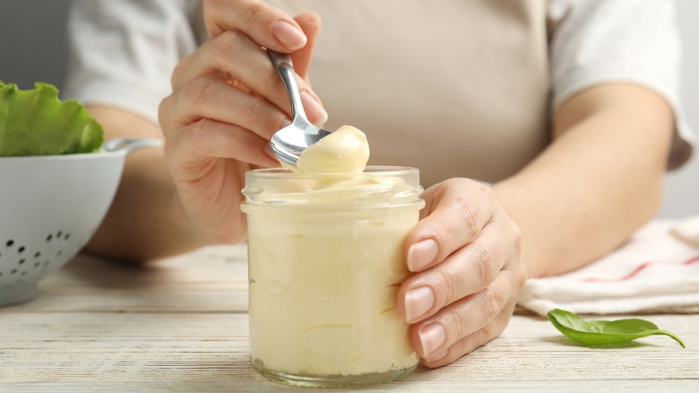 Person spooning out mayonnaise from jar