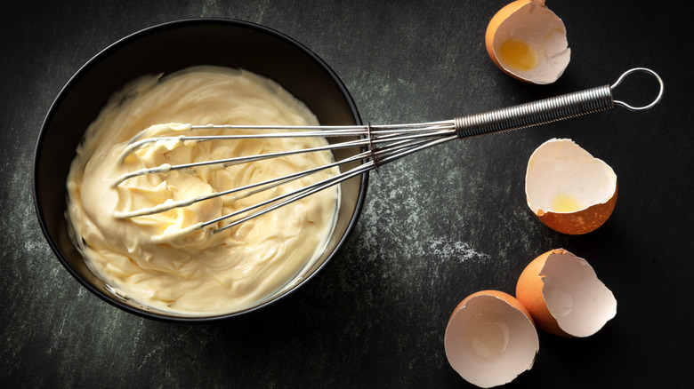 bowl of mayo with whisk near eggshells