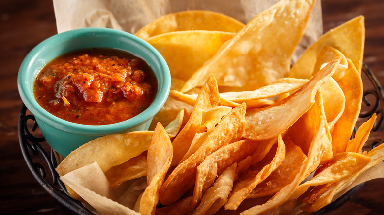 Basket of yellow corn tortilla chips with ramekin of tomato salsa