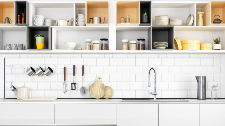 A white tiled kitchen with open shelving full of dishes and kitchenware