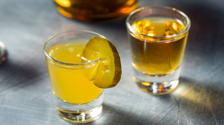 A shot of pickle juice garnished with one pickle chip and a shot of whiskey