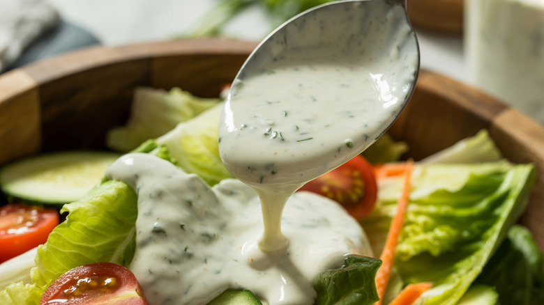 A spoon drizzles homemade ranch dressing onto a salad.