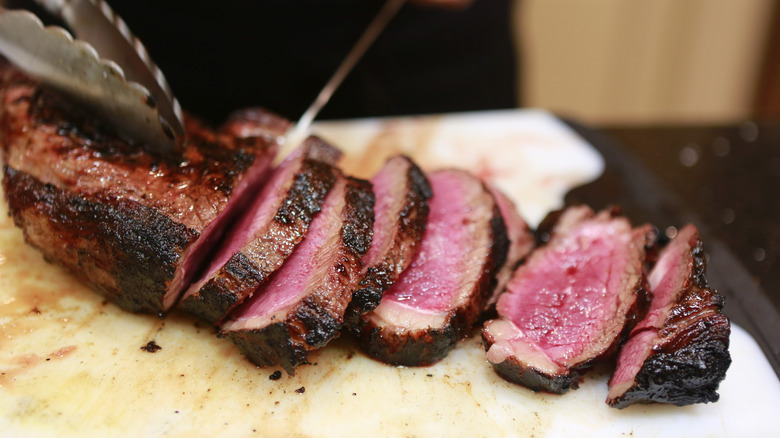 A piece of rare steak is cut into slices by a sharp knife