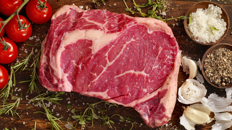 A raw ribeye surrounded by seasonings on a board