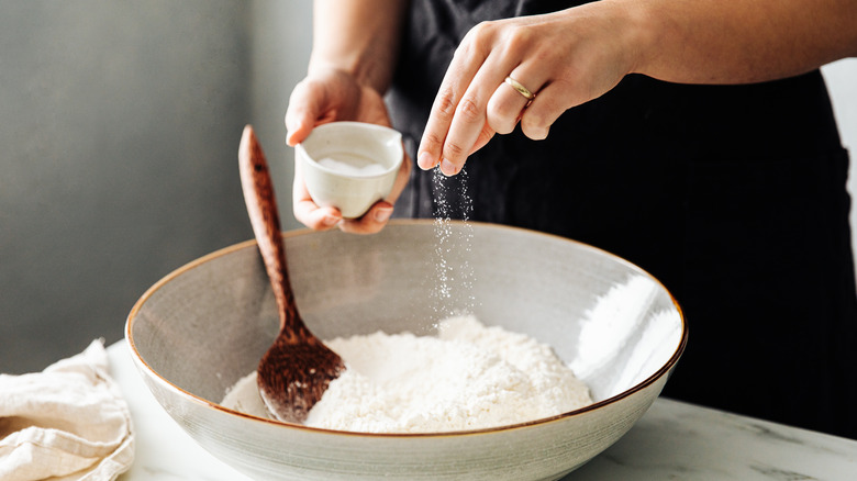 Person sprinkling salt in bowl of flour