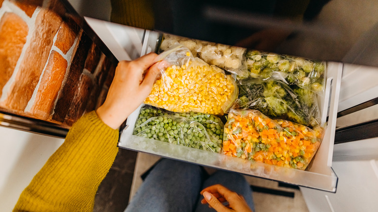 Hand takes a bag of frozen corn out of the freezer drawer