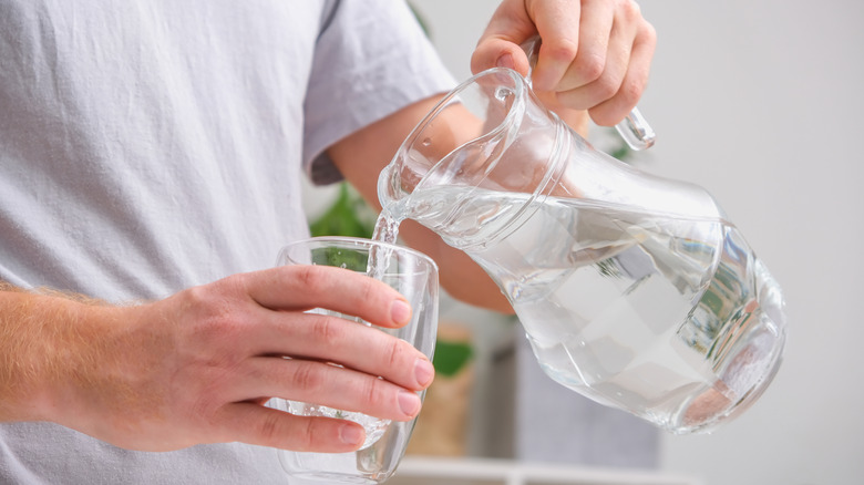 A person pouring a jug of water into a glass.