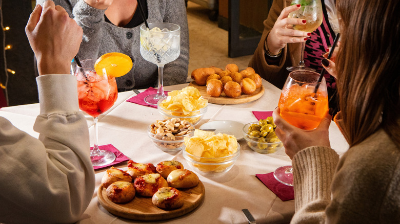 People sitting at a table with drinks and small plates of aperitivo food